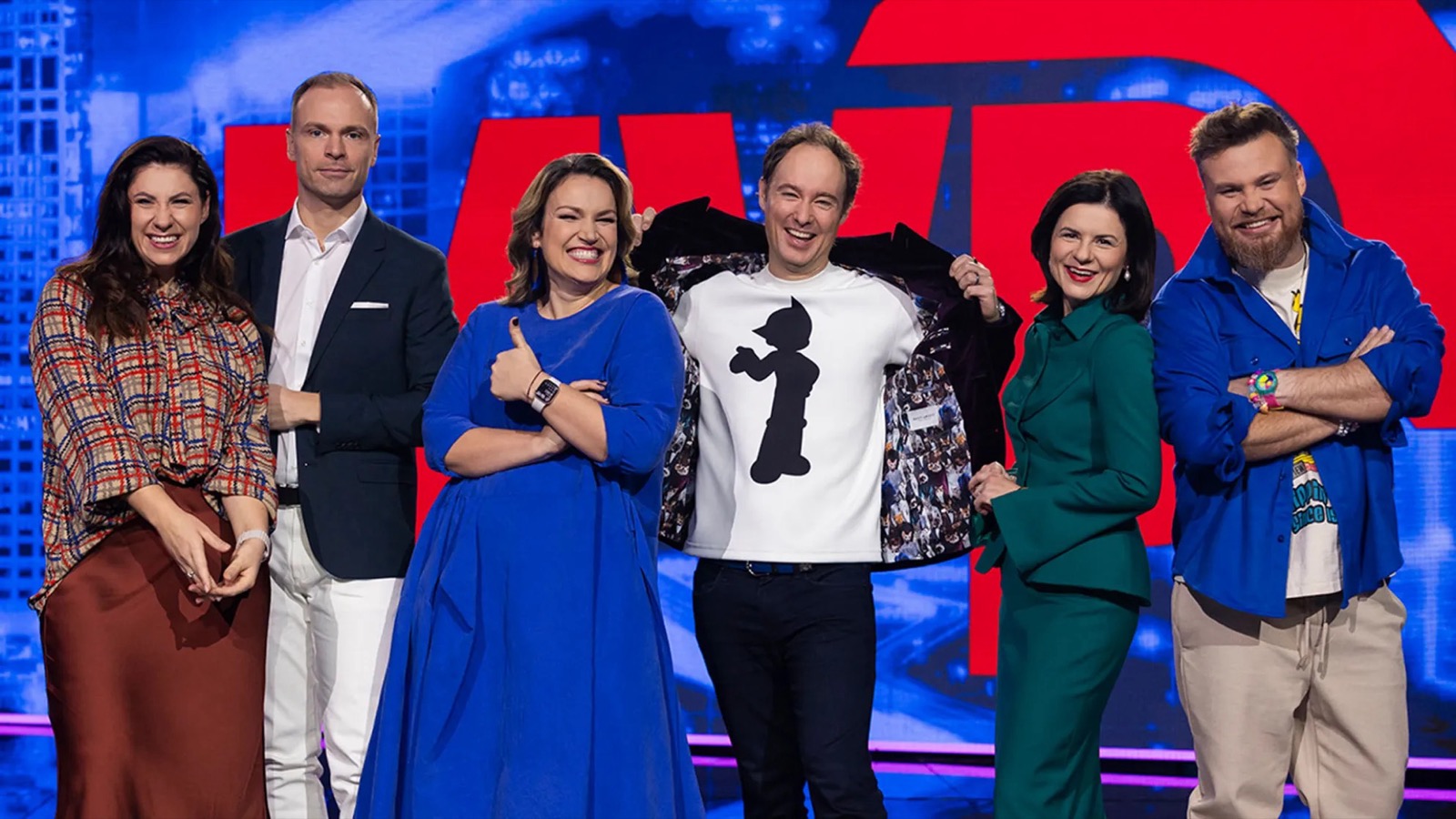 Martynas Kairys with the full MVP on TV3 cast lined up on the studio set, opening his jacket to reveal the show's mascot lining