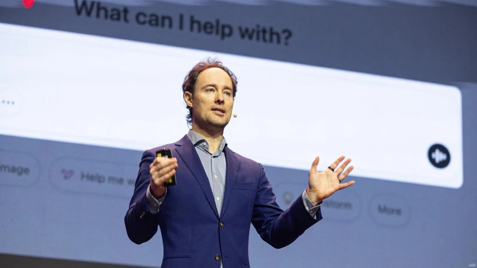 Martynas Kairys on stage at Sales Professionals Day, navy blazer, in front of a large AI chat interface screen