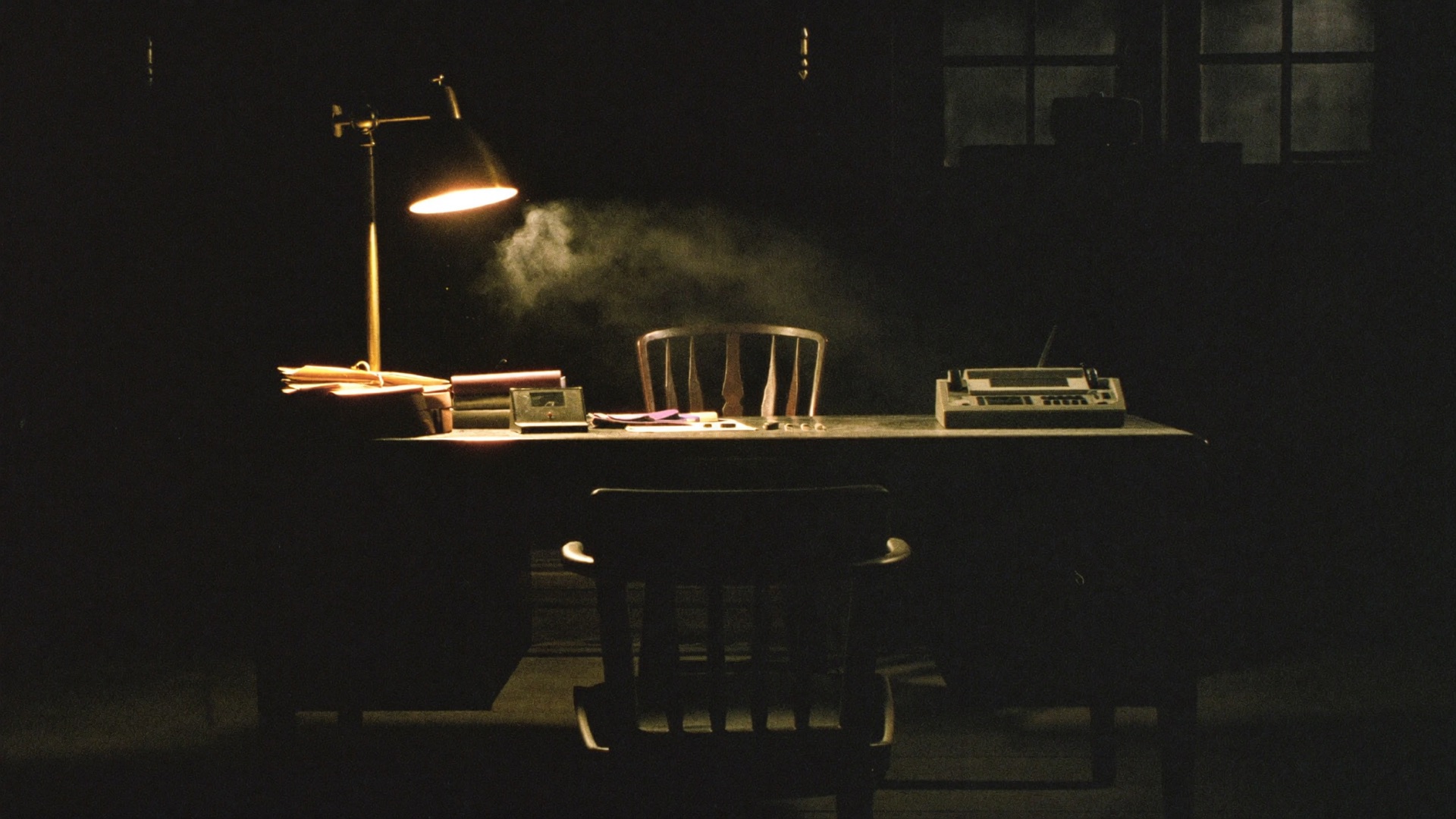 A scholar's desk lit by a single brass lamp in a dark wood-panelled study