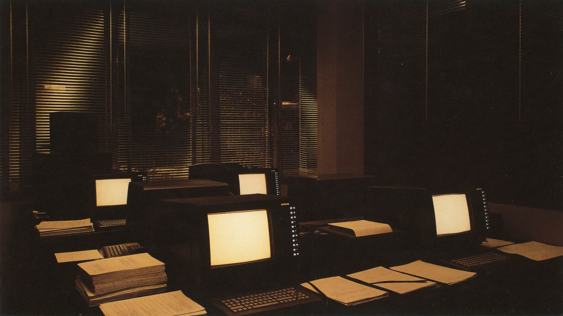 Rows of CRT terminals glowing amber in a dark 1980s office