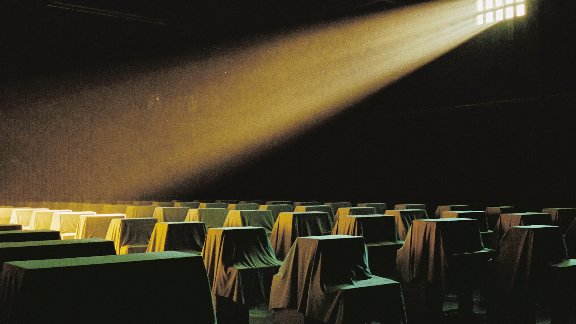 Computer workstations under pale dust covers in a dark warehouse, one shaft of golden light